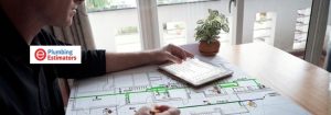 A plumbing estimator using a tablet to review project specifications over a detailed hydraulic layout blueprint on a desk.